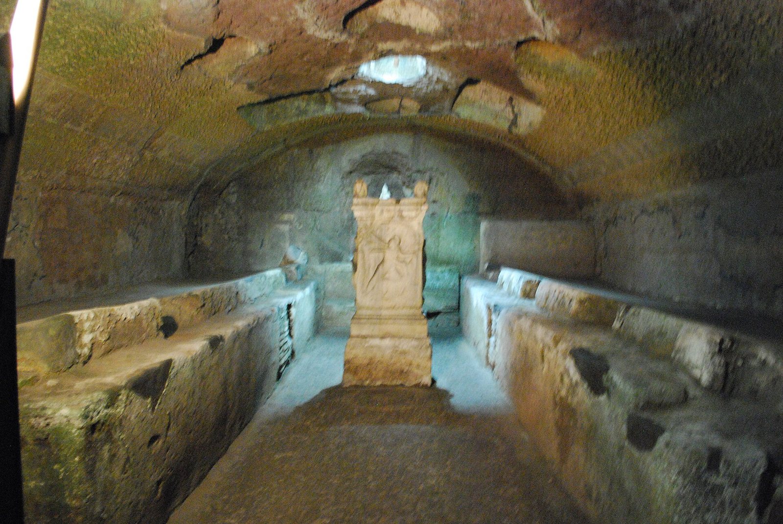 A dark underground Mithraic temple with stone benches and an altar, beneath the church of San Clemente in Rome.