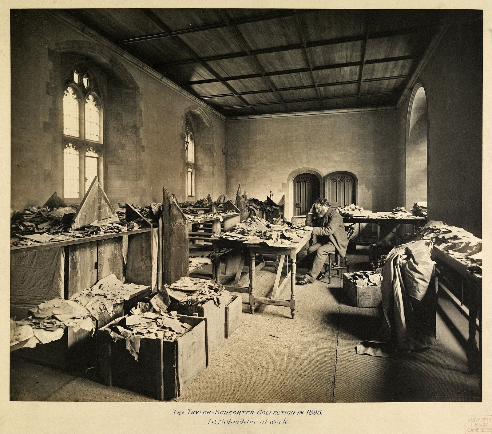Solomon Schechter at a long table covered with heaps of manuscript fragments from the Cairo Geniza.
