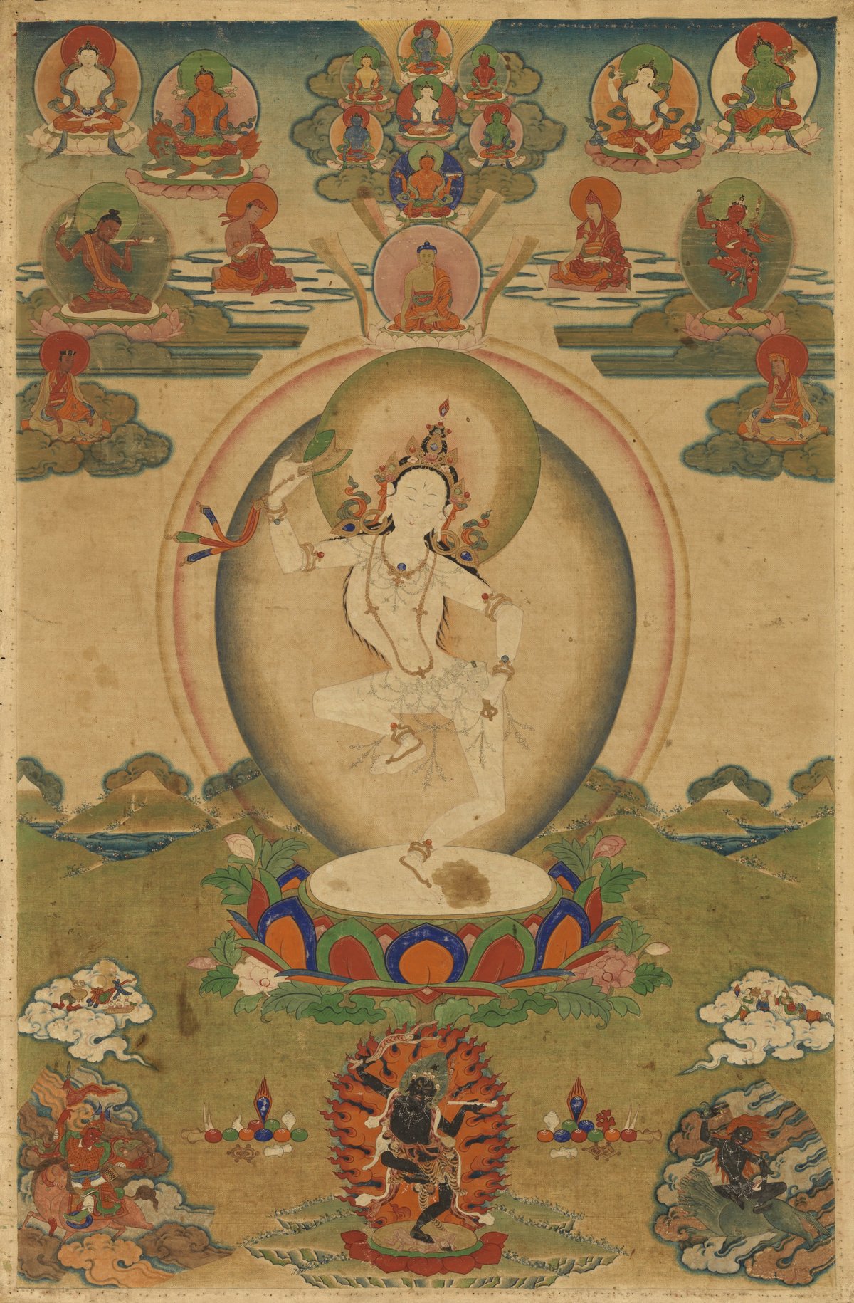 A Tibetan thangka painting of Machig Labdrön, white-bodied, dancing on one leg with a drum raised in her right hand, surrounded by buddhas, teachers and a black wrathful figure in flames.