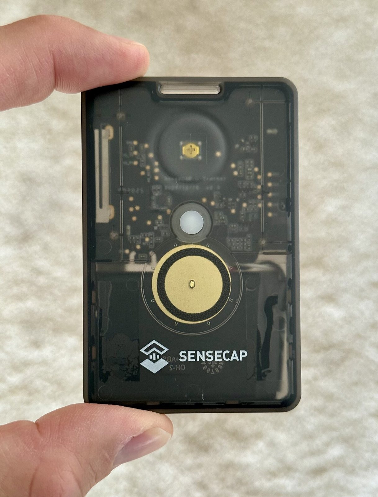 a credit-card-sized LoRa mesh tracker held between two fingers, its circuit board visible through the translucent case