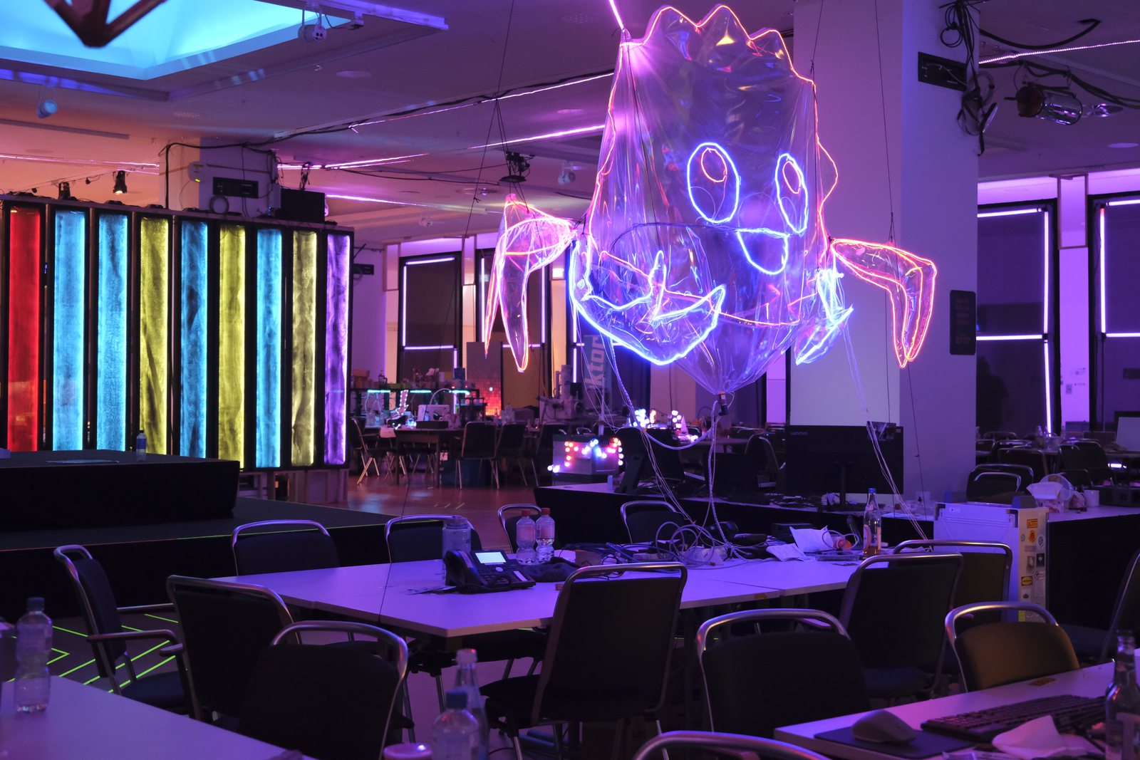 A large inflatable Ferris the crab outlined in neon light, hanging above desks at a hacker conference